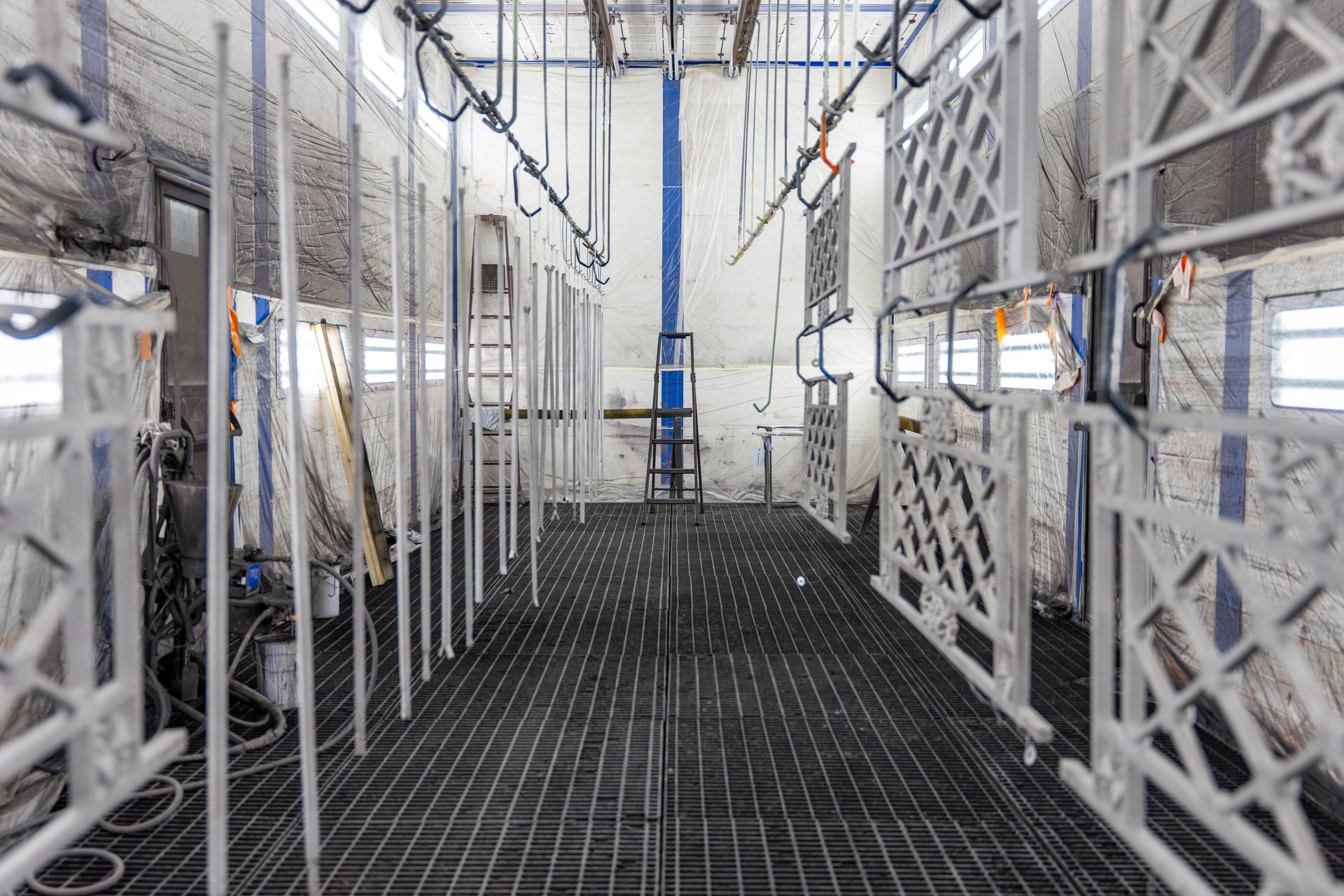 Intérieur d'une cabine de peinture métallique. Des cadres métalliques blancs sont suspendus à des rails suspendus.