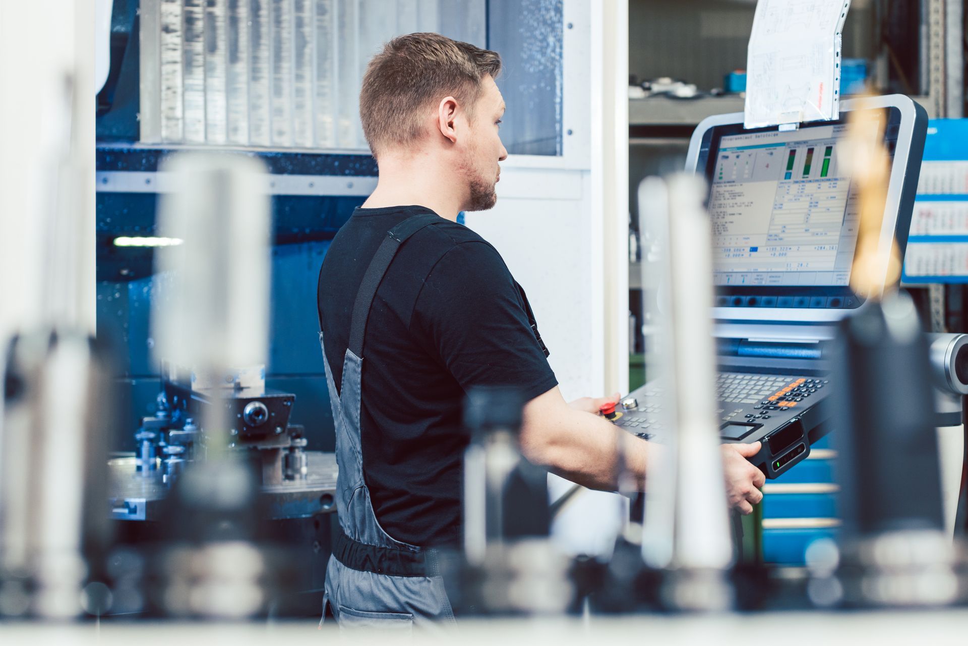 Homme utilisant une machine CNC dans un atelier ; aux tons bleus, avec des outils et un moniteur visibles.