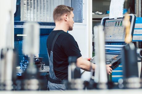 Homme utilisant une machine CNC dans un atelier ; aux tons bleus, avec des outils et un moniteur visibles.