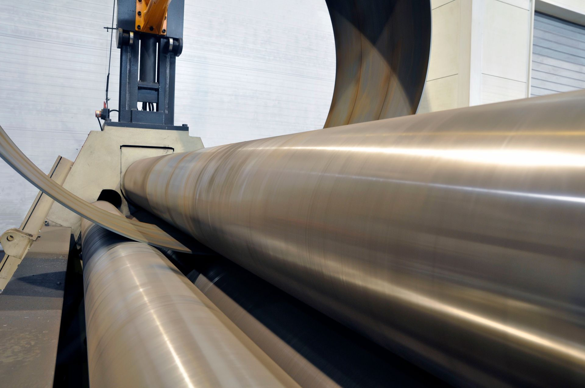 De grands rouleaux métalliques façonnent une tôle d'acier courbée dans une usine.