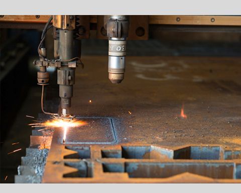 Un découpeur plasma coupant une feuille de métal, des étincelles jaillissent, dans un environnement industriel.