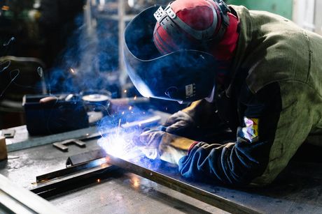 Soudeur portant un équipement de sécurité, soudant du métal dans un atelier, étincelles volantes.