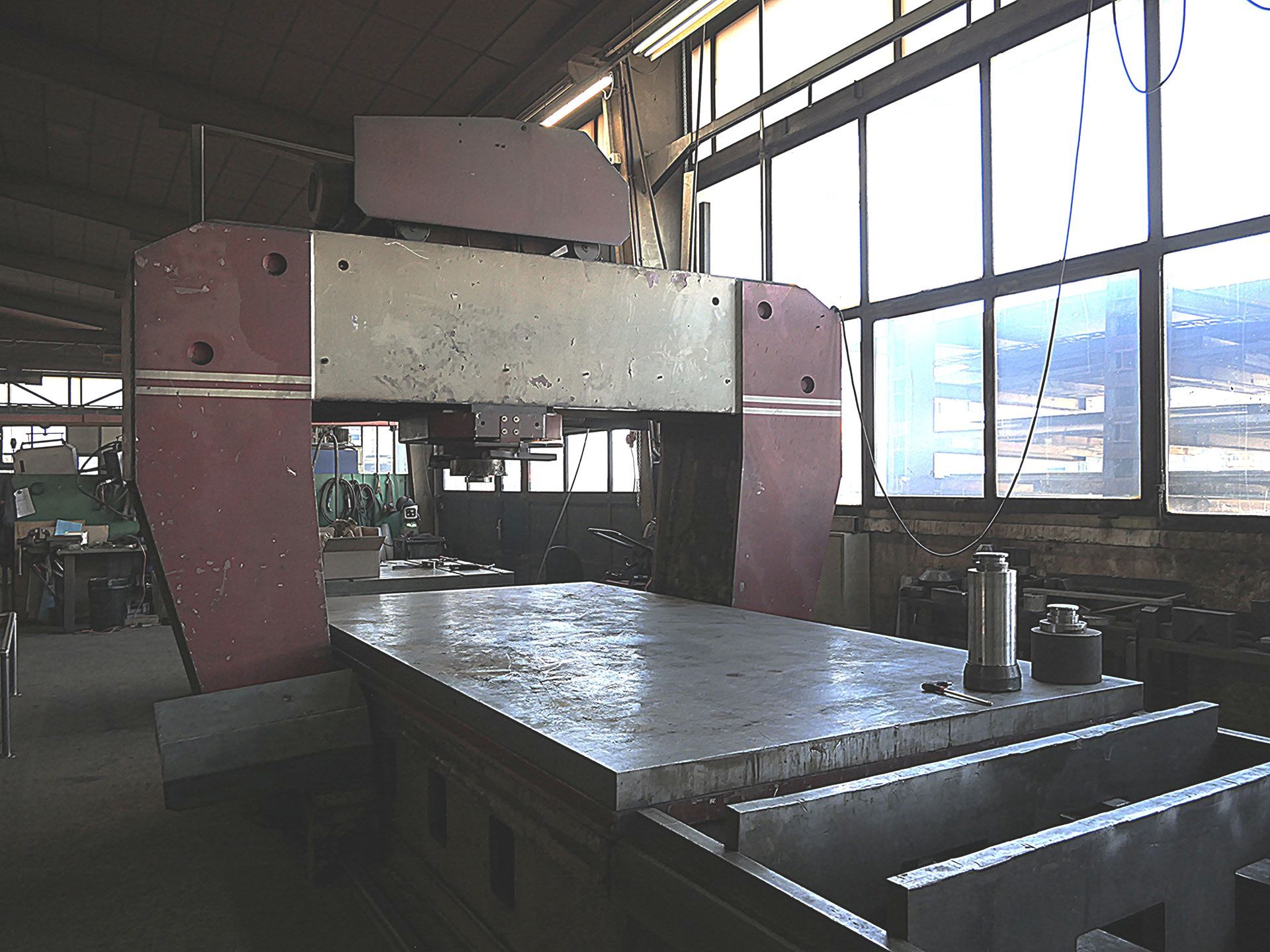 Presse industrielle jaune avec un bloc métallique et des pièces de machines à l'intérieur d'un atelier.