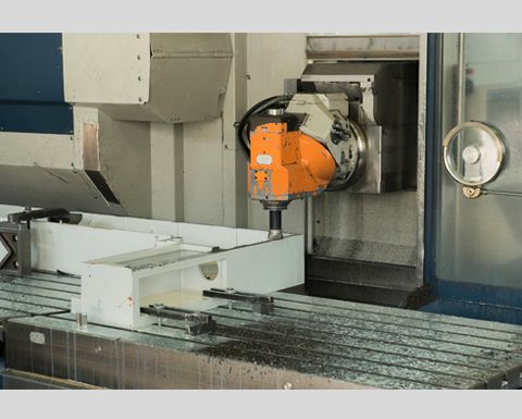Machine CNC fraisant une pièce métallique, la tête de machine orange perce un composant en métal blanc