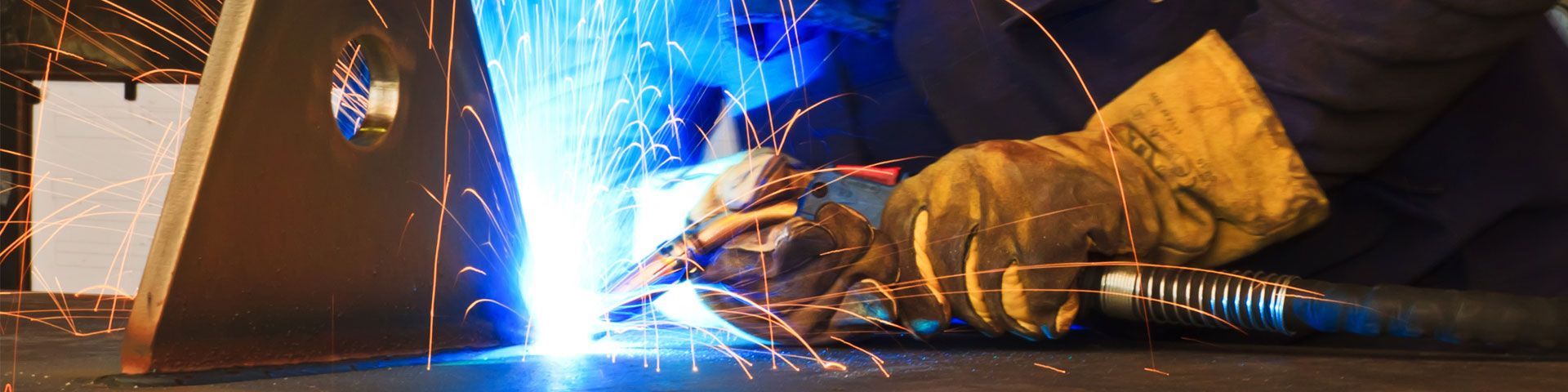 Une personne soude deux pièces métalliques ensemble. Une lumière bleue vive et des étincelles jaillissent.