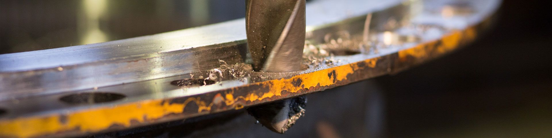 Un foret perce une bride métallique rouillée, créant des copeaux de métal.