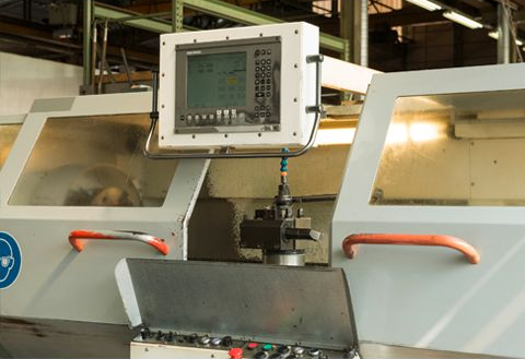 Machine CNC avec panneau de commande, poignées orange et verre de protection.