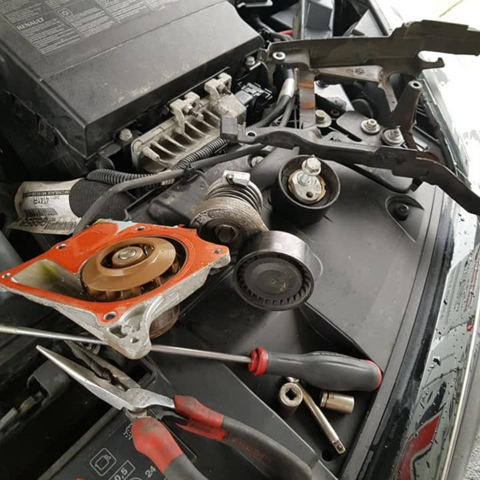 Des pièces de moteur de voiture éparpillées sur le moteur, des outils visibles.