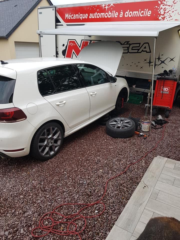 Voiture blanche, capot ouvert, pneu démonté, garée à côté d'une camionnette de mécanicien mobile.