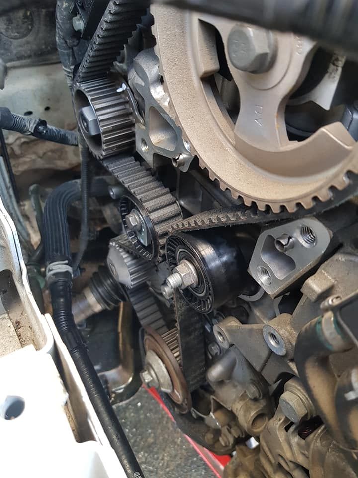 Moteur avec courroie de distribution et poulies. Courroie noire sur les pignons. Composants gris et noirs.