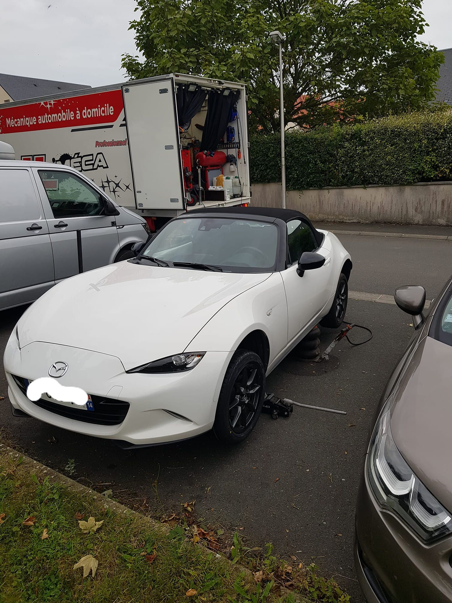 Une voiture décapotable blanche à jantes noires est en cours de réparation à côté d'une camionnette d'assistance blanche.