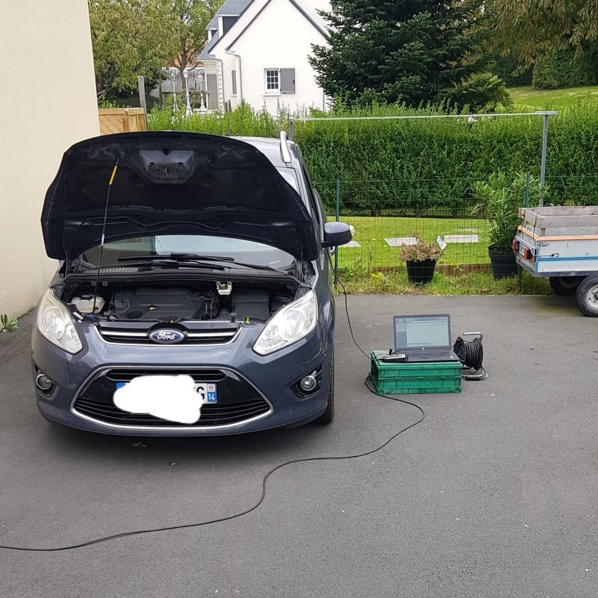 Voiture Ford, capot ouvert, connectée à un ordinateur portable et à du matériel, garée dans une allée.