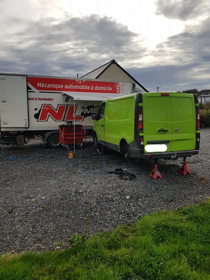 Fourgonnette verte sur chandelles, garée à côté d'un camion d'assistance. Outils et pneus au sol. Ciel nuageux.