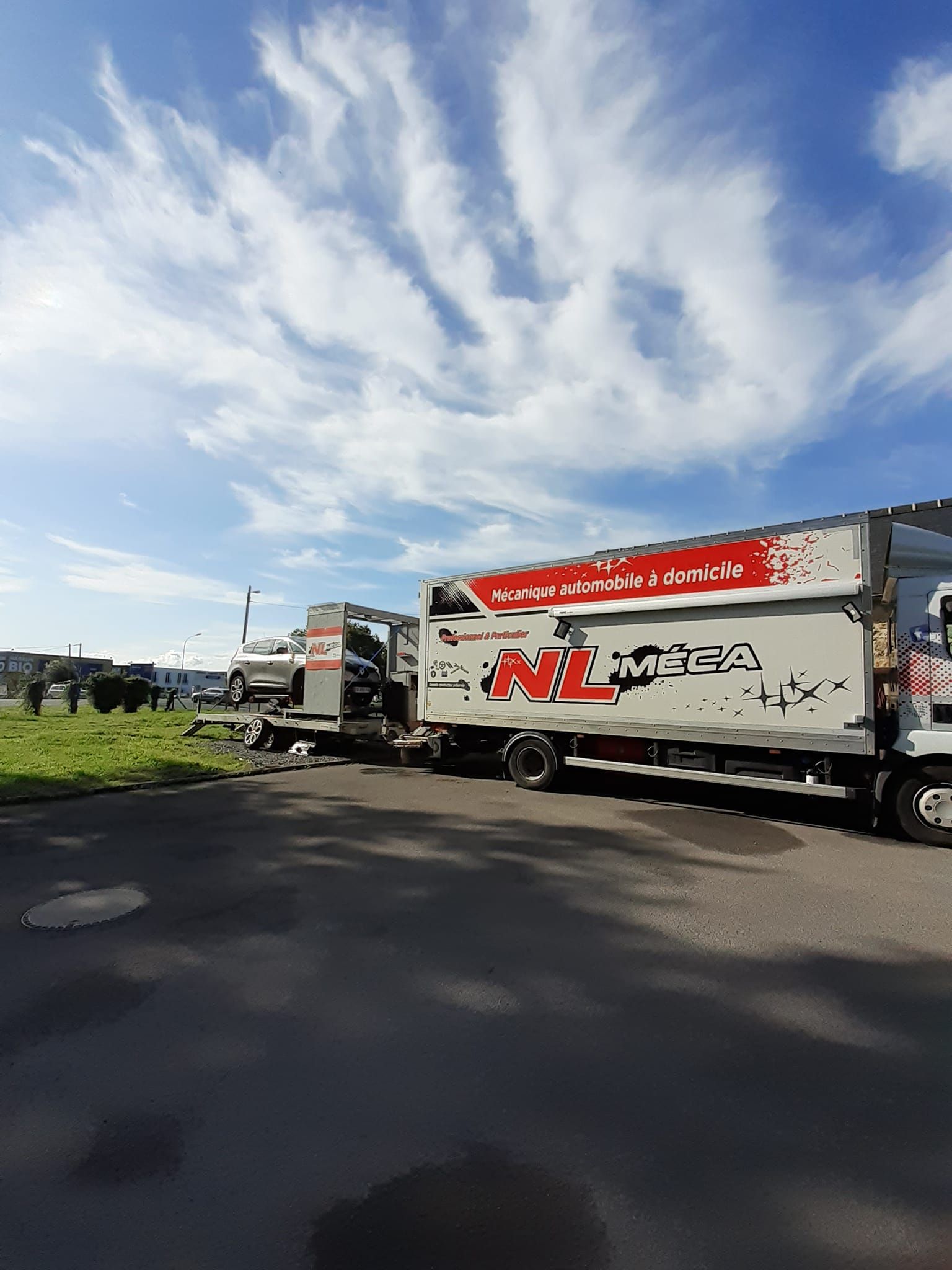 Deux camions blancs avec des logos rouges garés sur l'asphalte sous un ciel bleu nuageux.