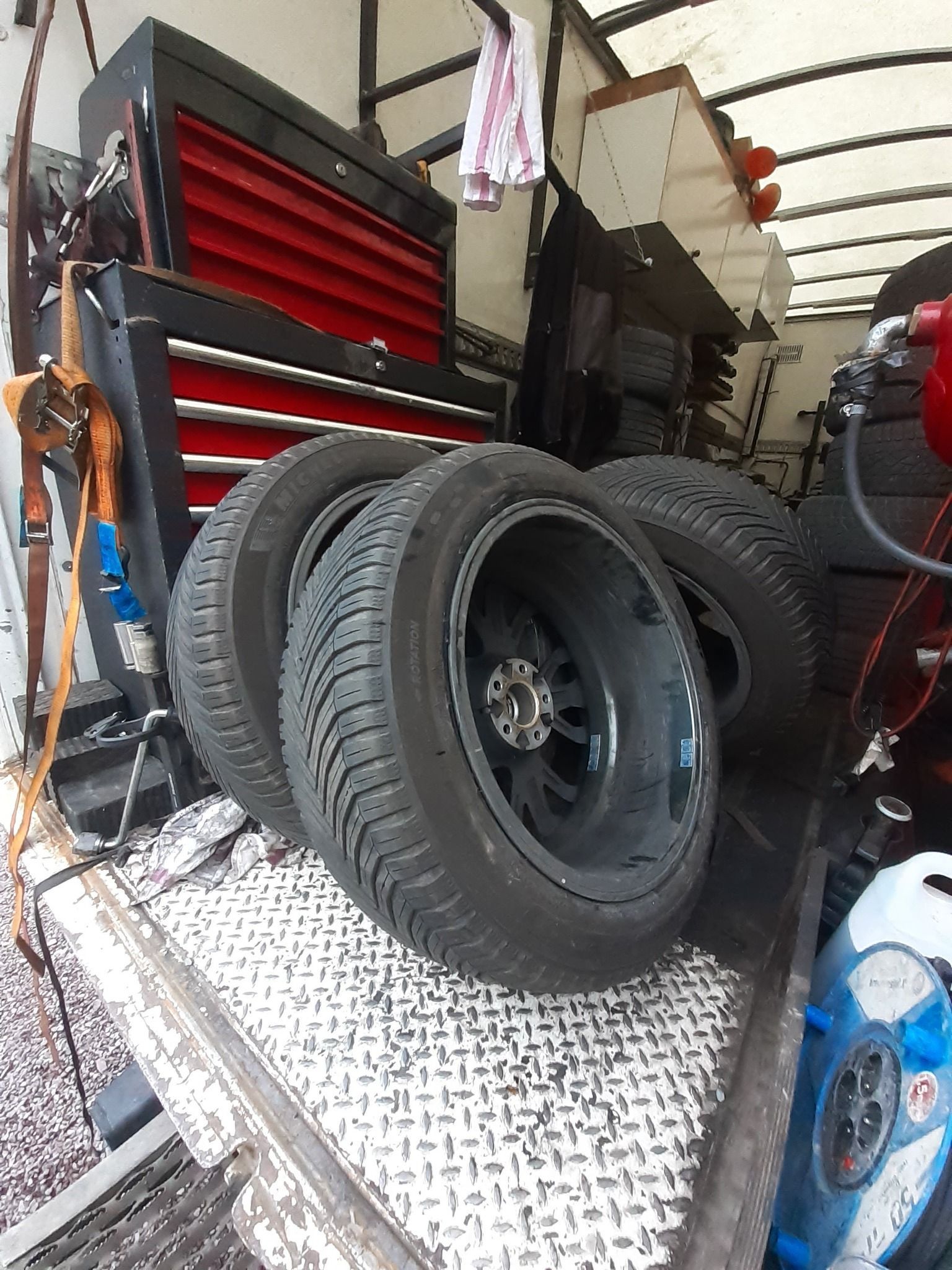 Quatre pneus à jantes noires à l'intérieur d'un camion avec une boîte à outils.