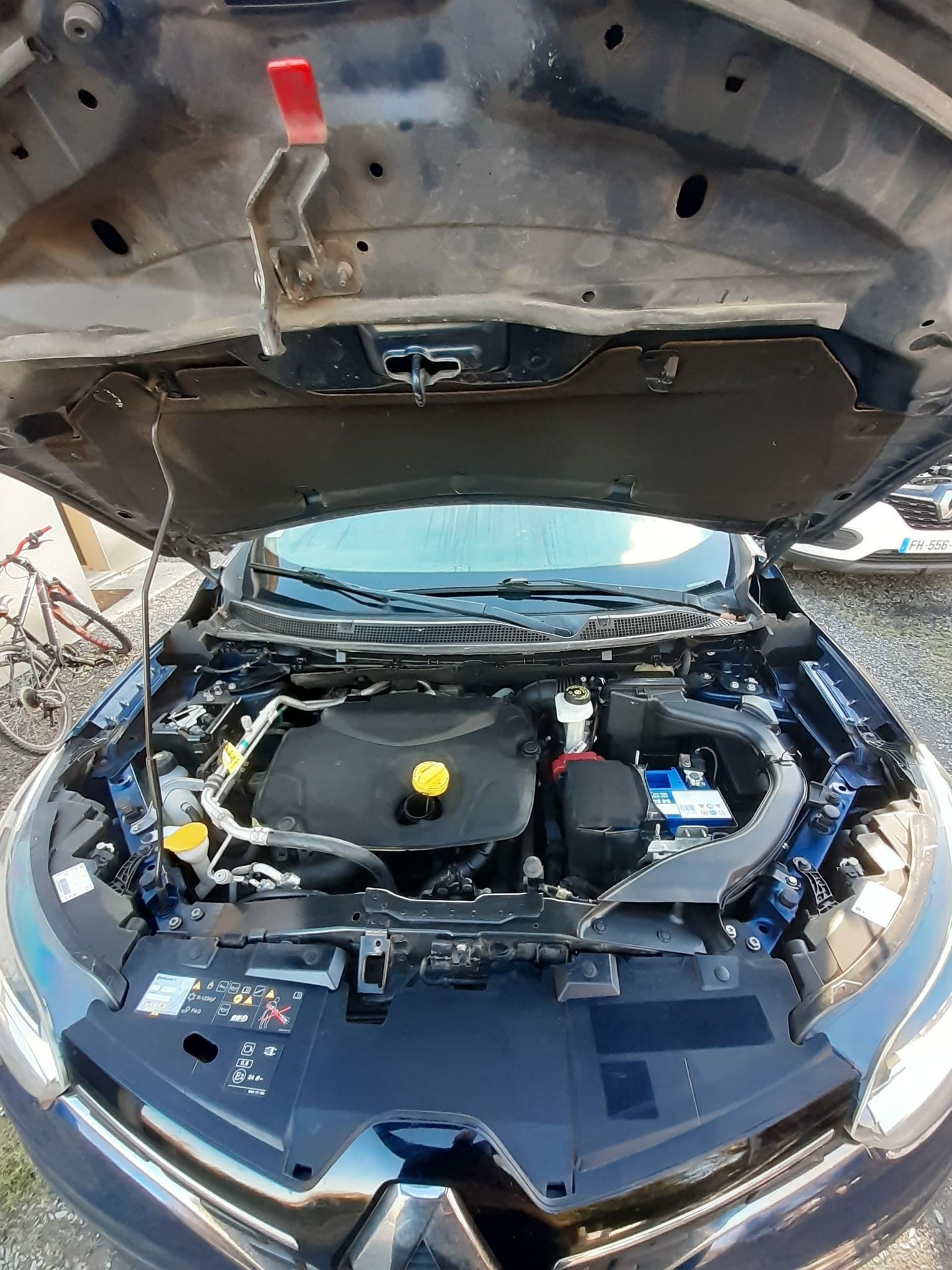 Compartiment du moteur d'une voiture bleu foncé, capot ouvert. Le moteur est visible, avec sa batterie et ses différents composants.
