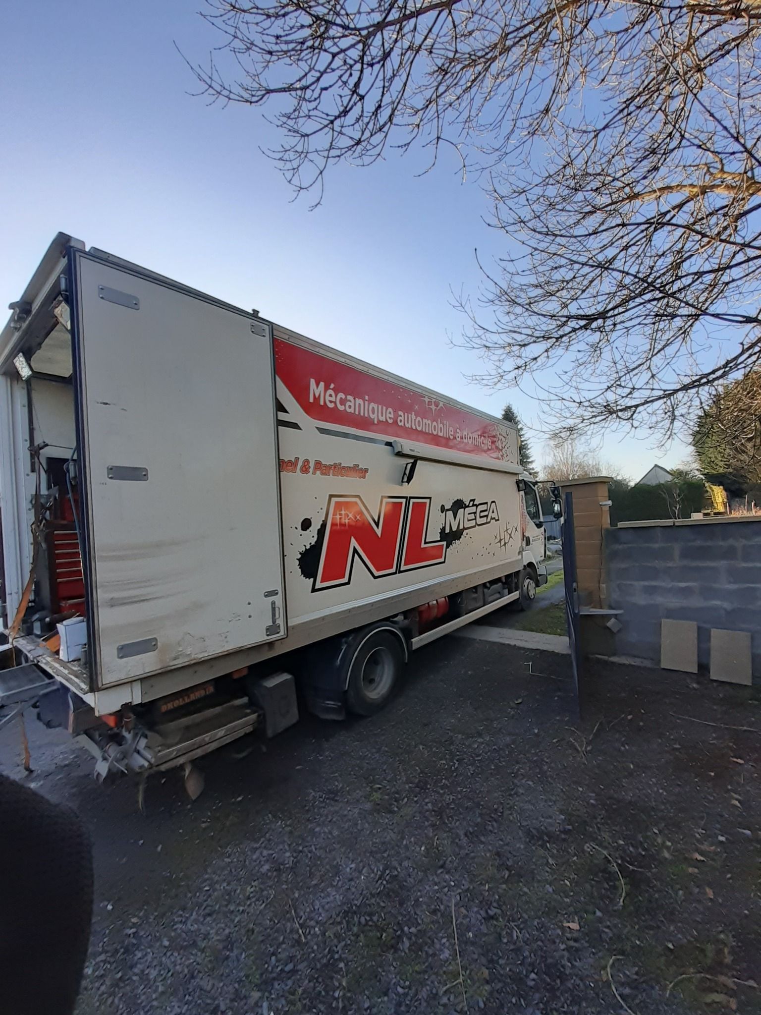 Un gros camion de livraison blanc portant le logo NL est stationné à l'extérieur.
