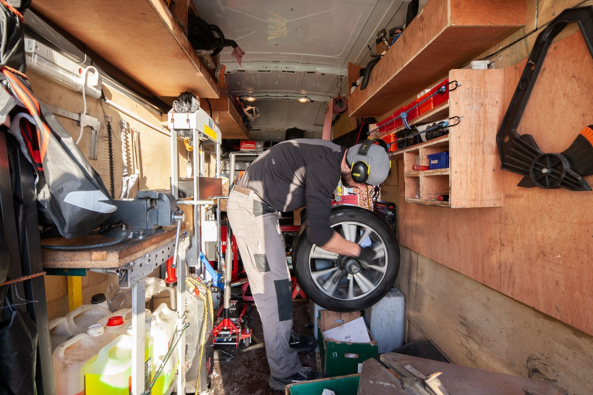 Un homme range des outils et un pneu dans une camionnette. Des étagères tapissent les murs.