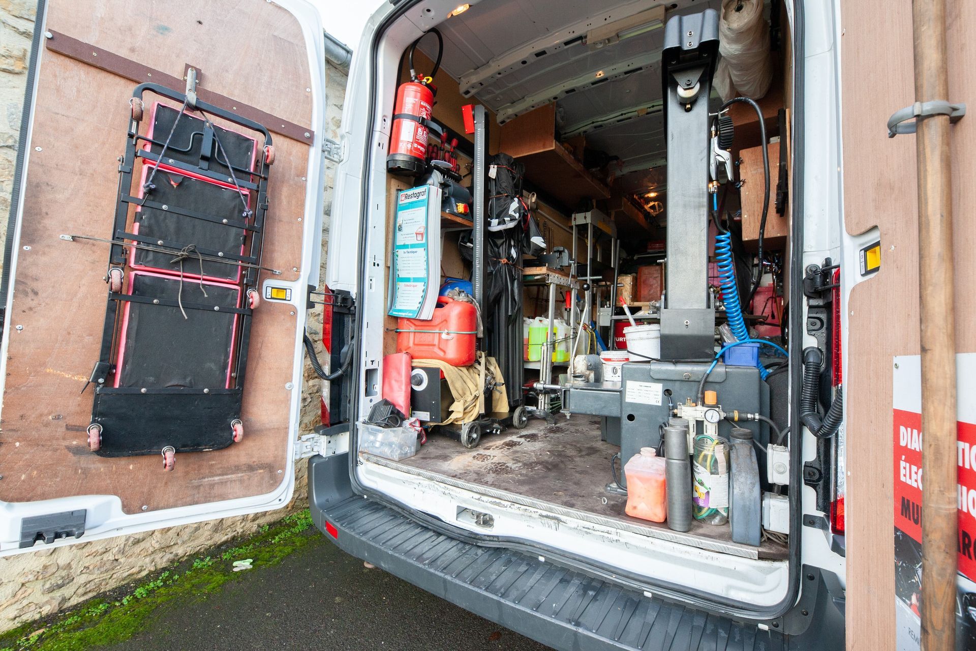 L'arrière ouvert d'une camionnette blanche remplie d'outils, d'équipements et d'étagères de rangement.