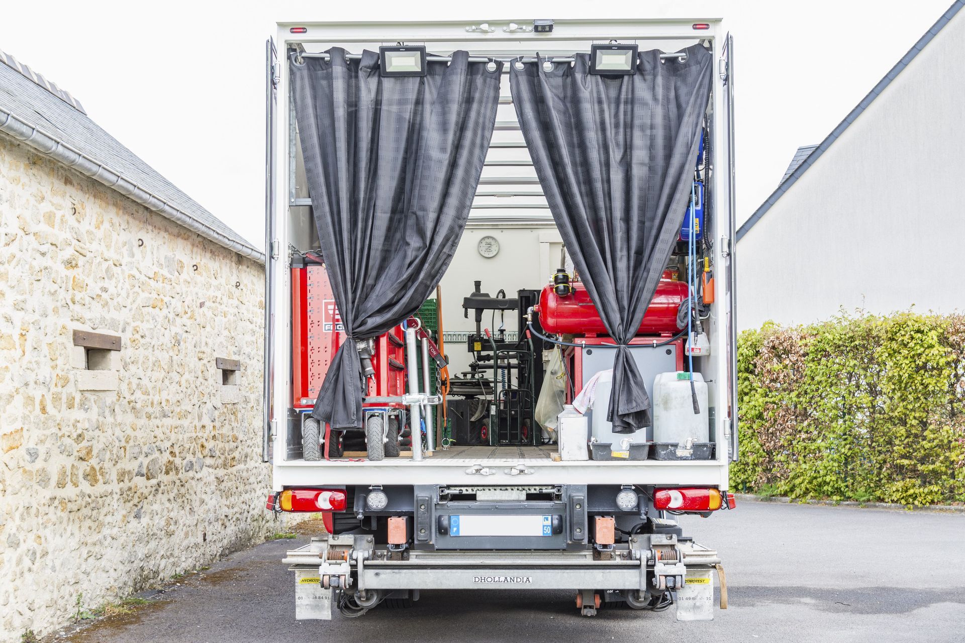 L'arrière d'un camion d'assistance est ouvert, laissant apparaître outils et équipements. Des rideaux gris obstruent partiellement la vue.