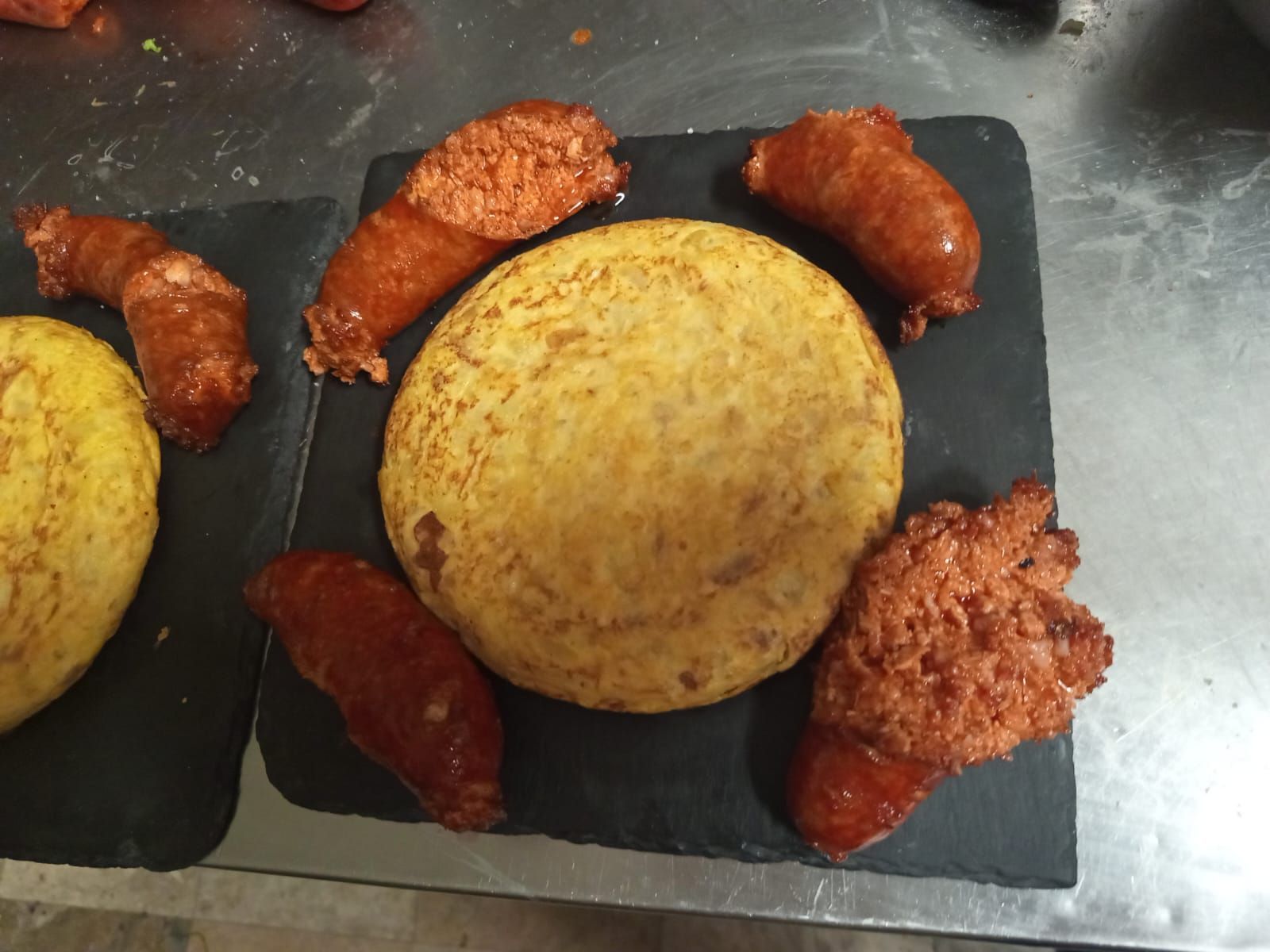 Plato con tortas de arroz redondas de color amarillo y trozos de pollo frito rojo en bandejas negras.