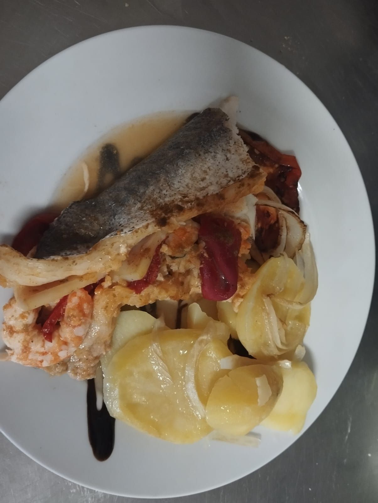 Pescado emplatado con patatas y verduras en una salsa ligera sobre un plato blanco.