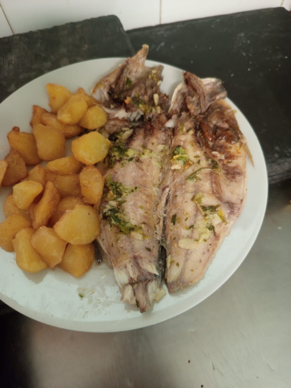 Plato con pescado asado y trozos de patata dorada sobre un plato blanco.