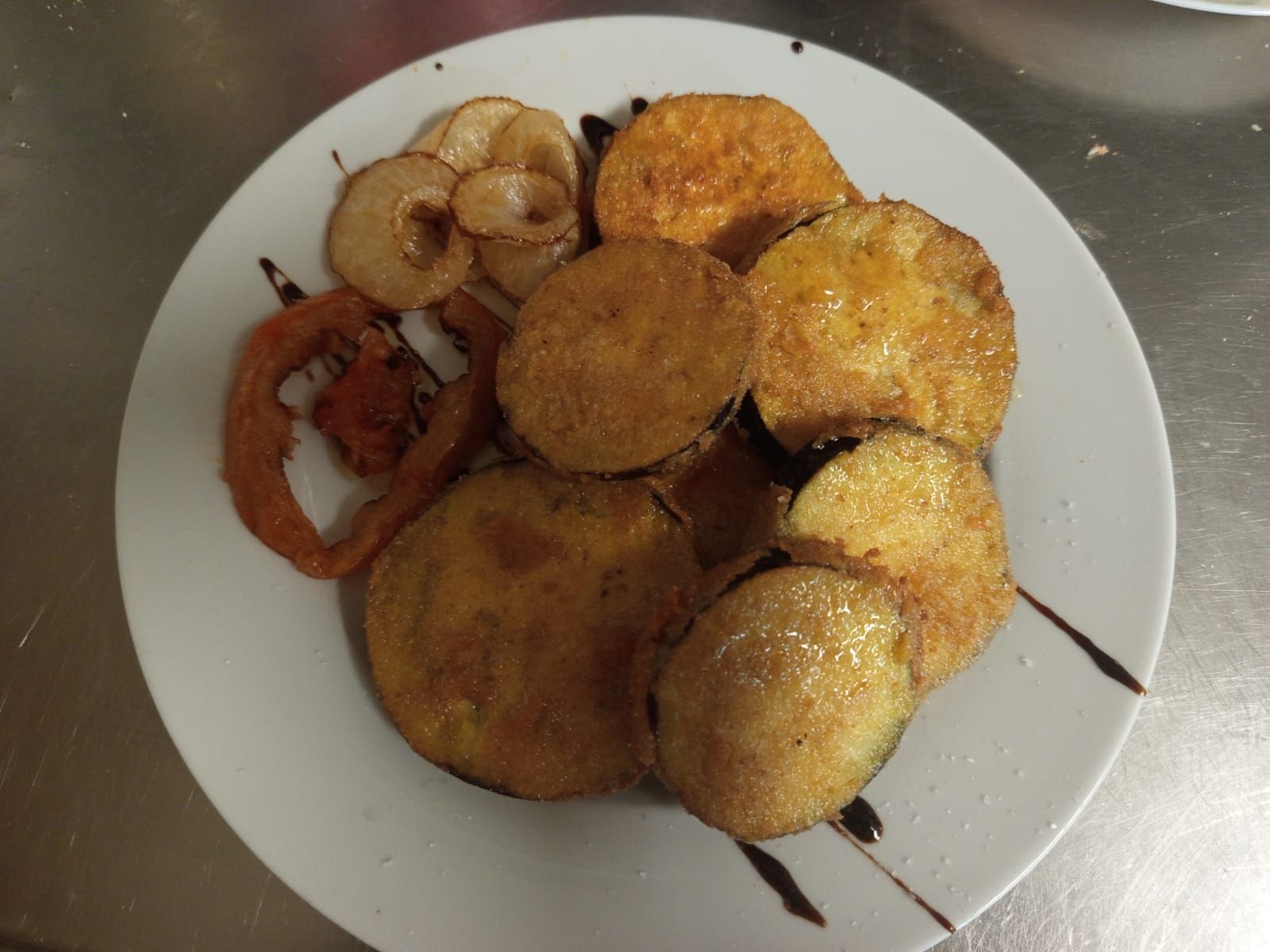 Plato de aperitivos fritos variados sobre una mesa de metal, que incluye piezas redondas doradas y marrones y anillos.