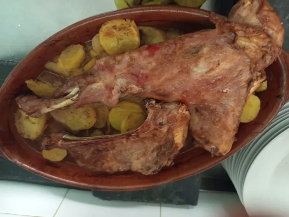 Conejo entero asado en una fuente marrón con patatas y cebollas en rodajas.