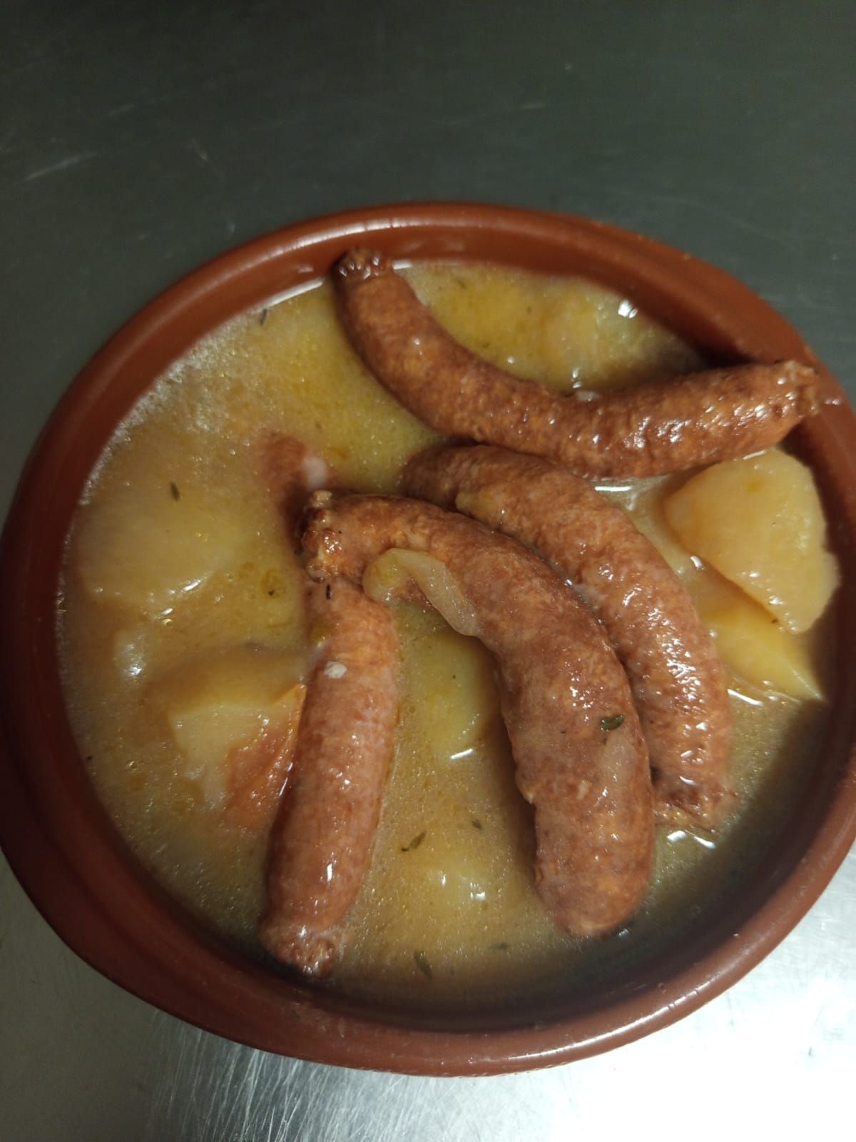 Un tazón de sopa amarilla cubierto con varias salchichas doradas sobre una superficie metálica.