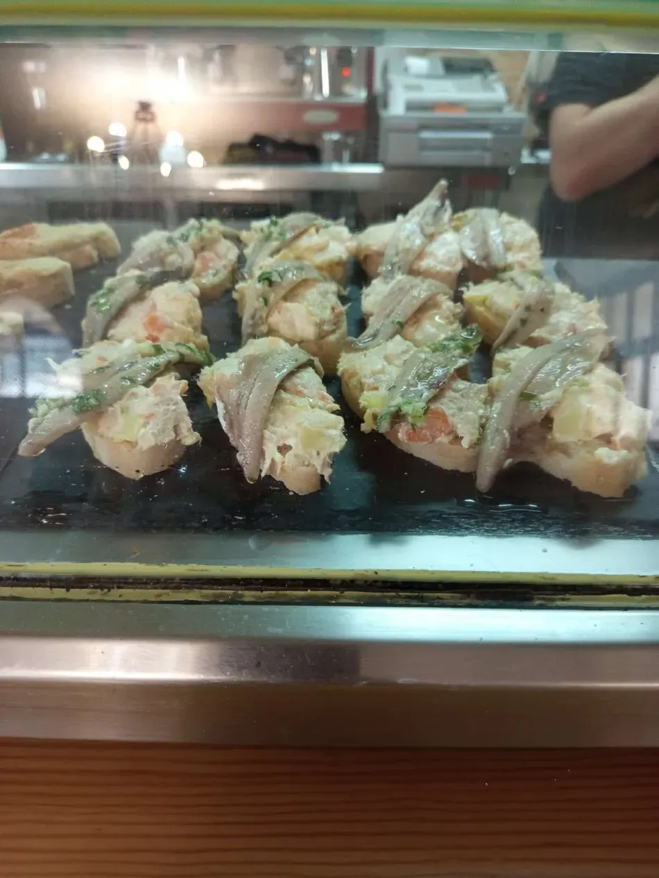 Bandeja de rollos de sushi en una vitrina de cristal, cubiertos con salsa blanca y guarniciones.