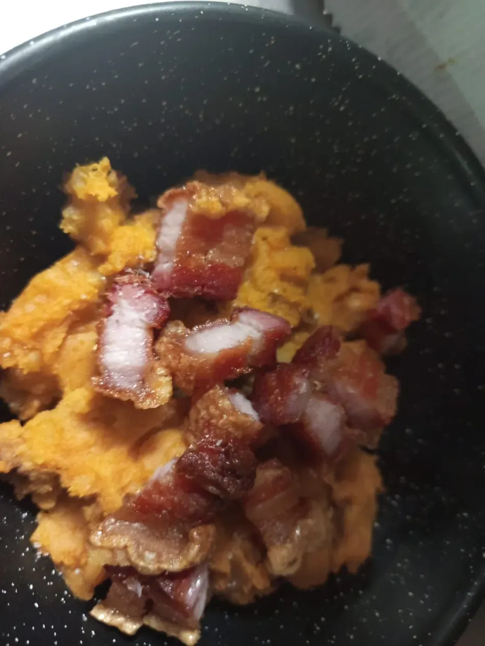 Primer plano de un tazón de puré de naranja cubierto con trozos de tocino crujiente.