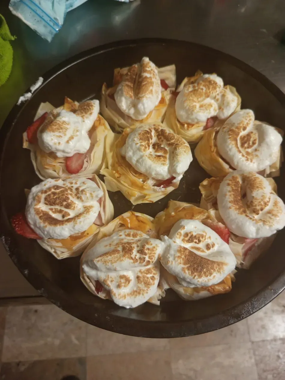 Plato de pasteles horneados cubiertos con espirales de crema y canela sobre una bandeja oscura.