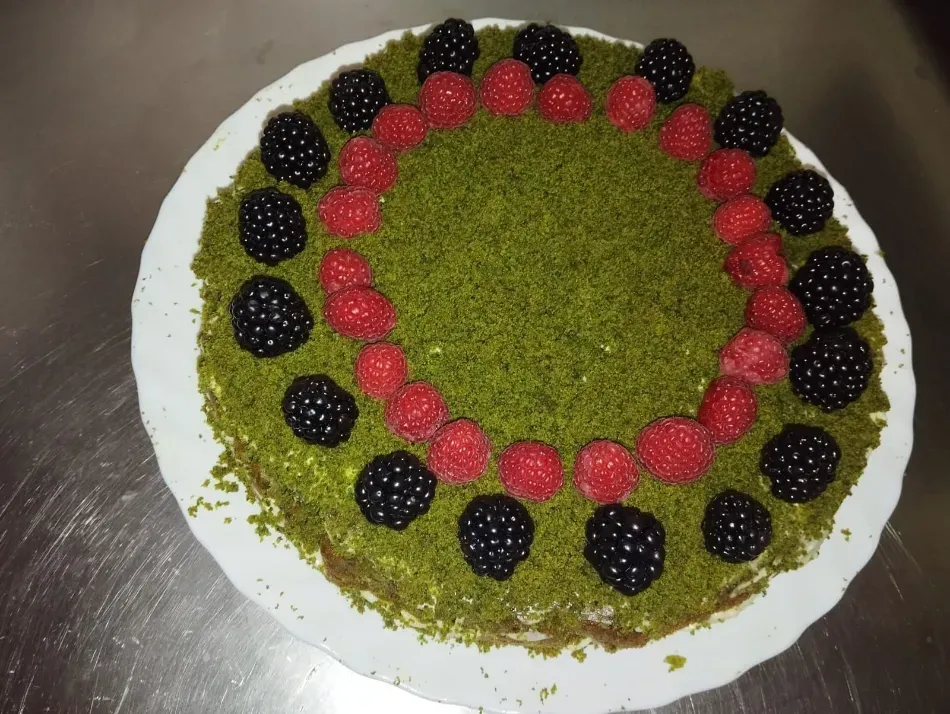 Pastel redondo verde decorado con bayas rojas y negras sobre un plato blanco.