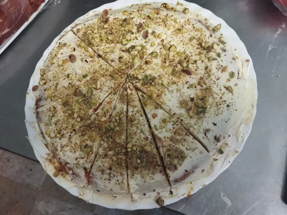 Pizza redonda cubierta con hierbas y queso, cortada en porciones sobre una bandeja.