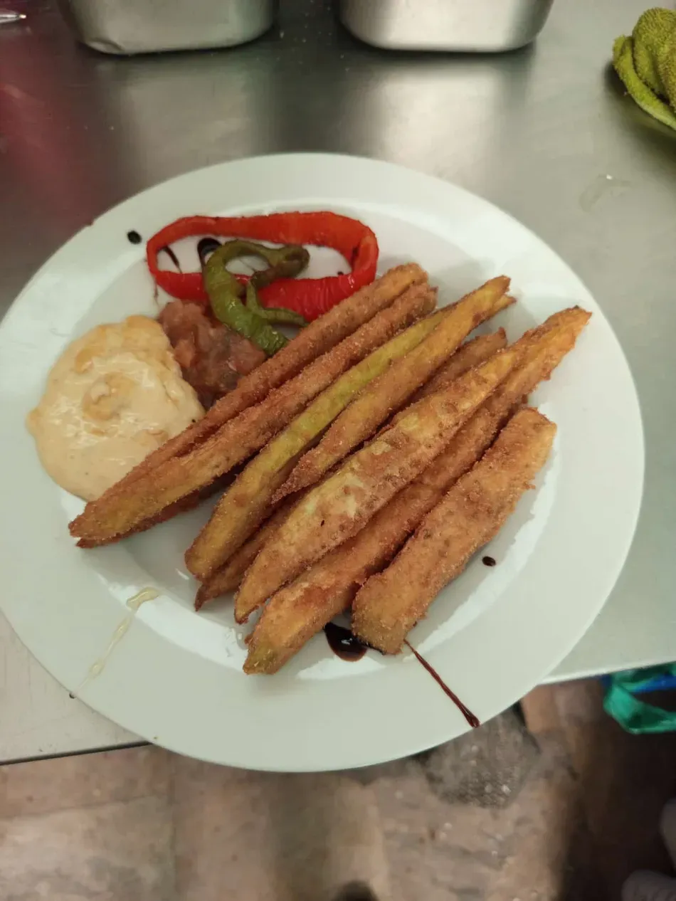 Palitos fritos servidos en un plato blanco con pimientos en rodajas y una salsa para mojar.