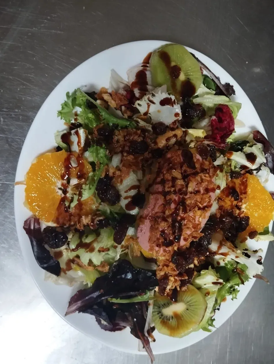 Ensalada mixta con pollo a la parrilla, rodajas de naranja, kiwi y un chorrito de vinagre balsámico en un plato blanco.