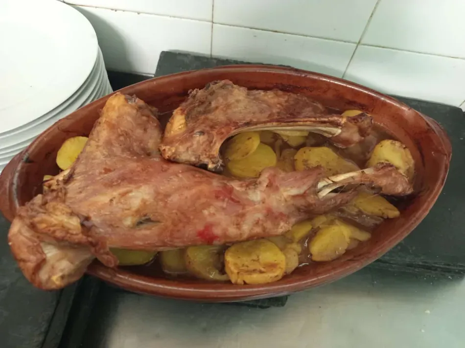Carne asada con patatas en una fuente ovalada marrón sobre la encimera de la cocina.