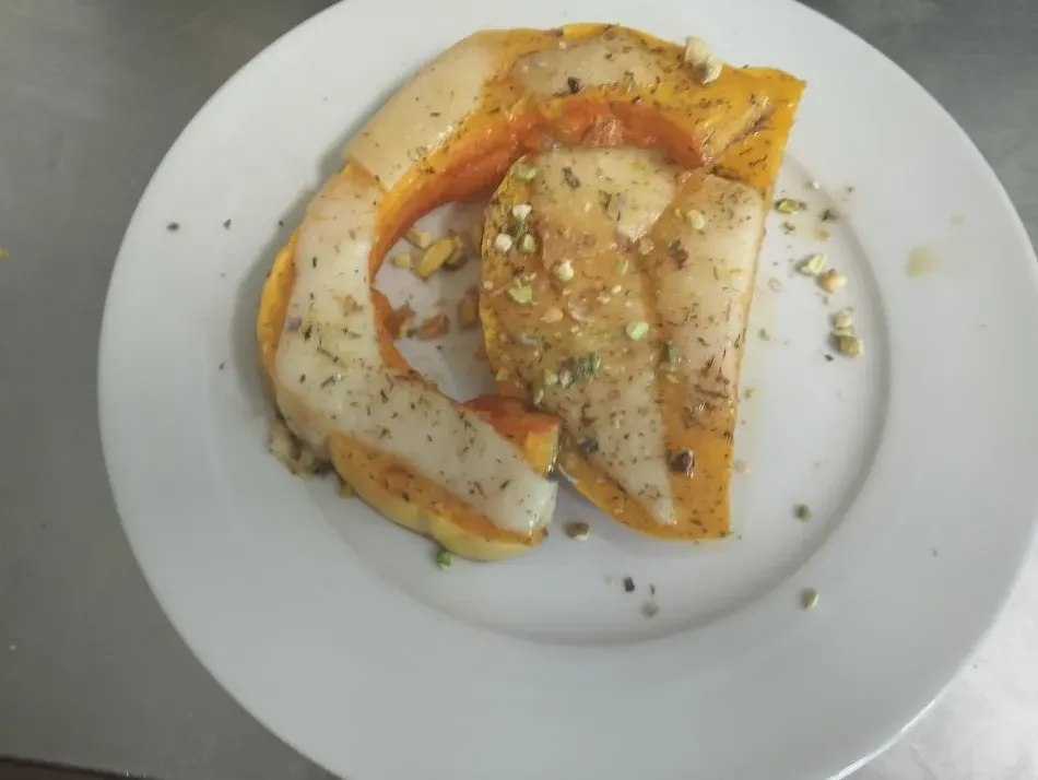 Calabaza asada en rodajas con condimentos sobre un plato blanco.