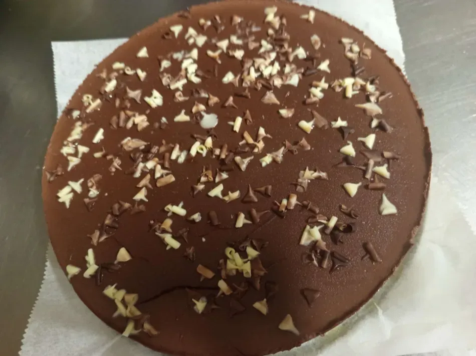 Pastel redondo de chocolate cubierto con virutas de chocolate blanco y negro sobre una servilleta blanca.