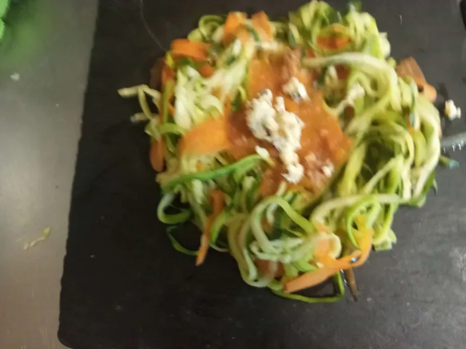 Ensalada de fideos de calabacín con verduras naranjas y queso blanco en un plato negro.