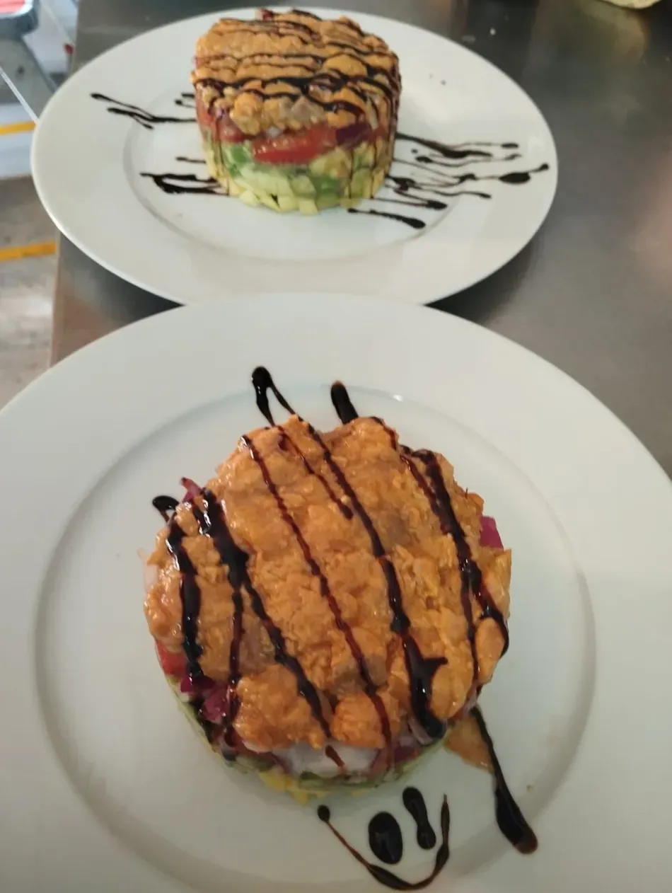 Dos postres en capas servidos en platos y bañados en salsa de chocolate sobre una mesa.