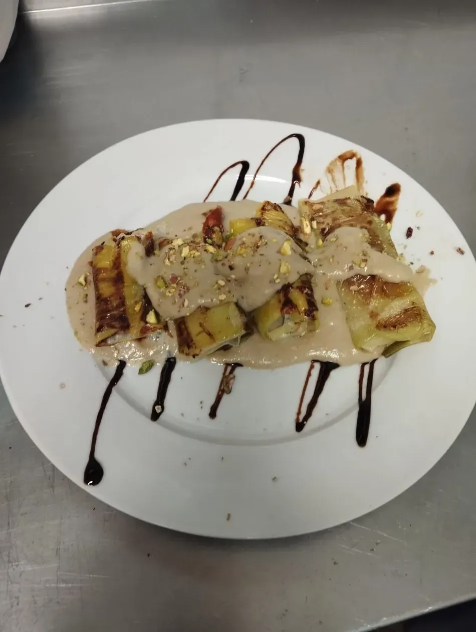 Plato de crepes de postre bañados en chocolate y crema sobre una mesa de acero inoxidable.