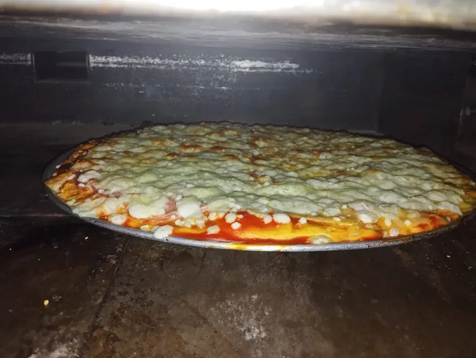 Pizza de queso horneándose en un horno, con queso derretido y salsa roja en los bordes.
