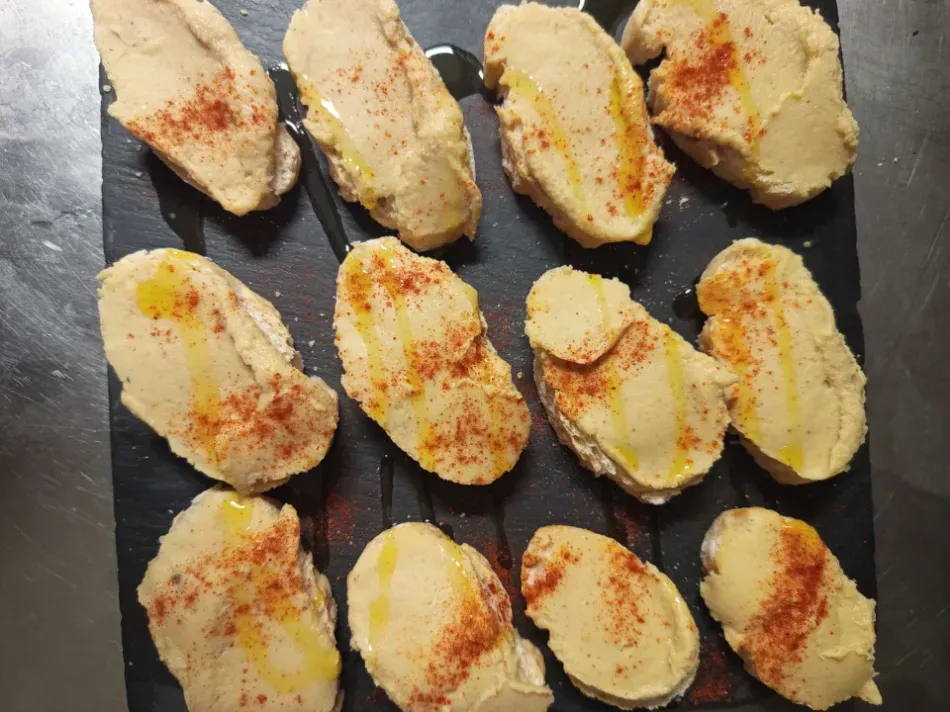 Rebanadas de pan untadas con mantequilla y especias rojas sobre una tabla de pizarra oscura.