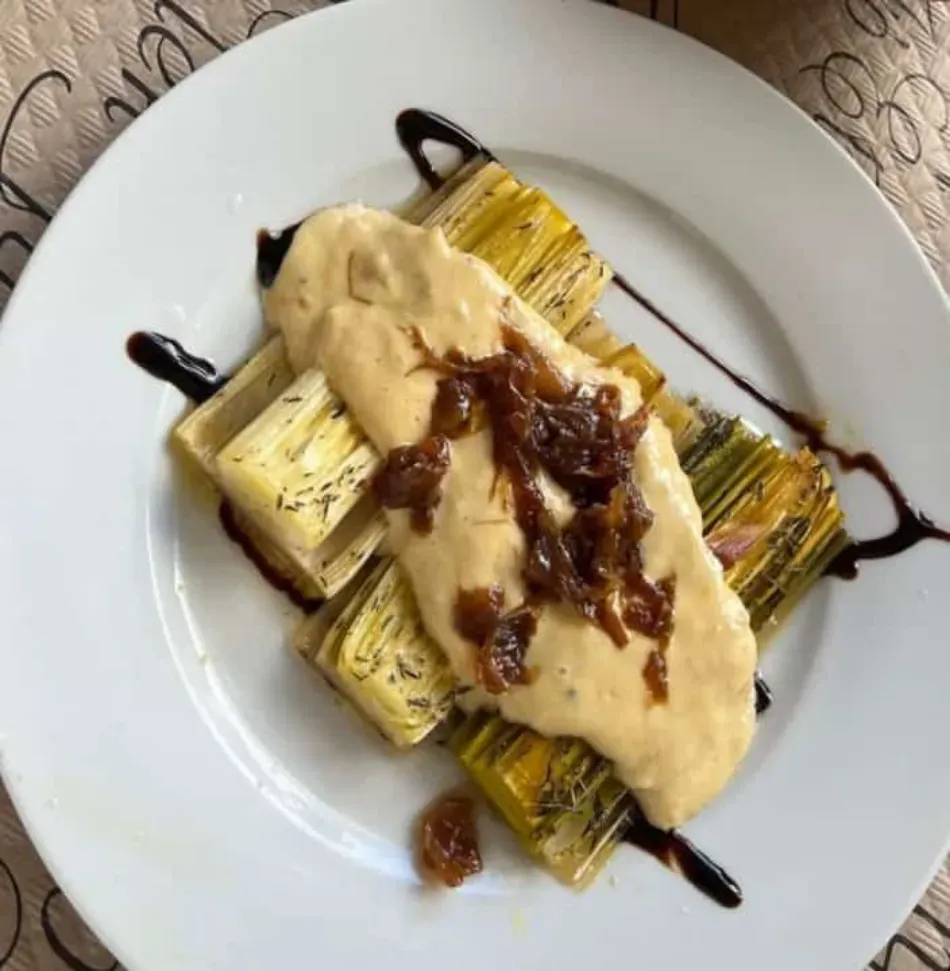 Maíz a la parrilla en un plato blanco con salsa cremosa y guarnición oscura rociada.