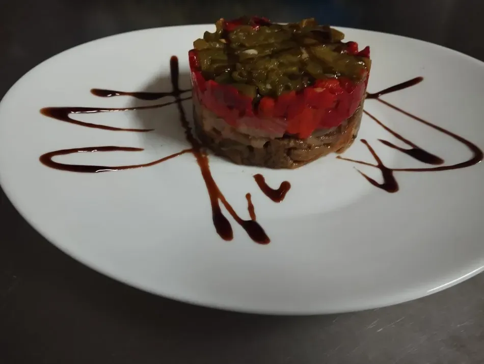 Tarta de postre con cobertura roja y verde, bañada en chocolate sobre un plato blanco.
