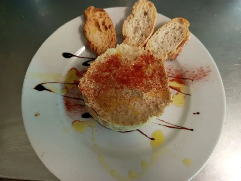 Bola de queso empanizada en un plato blanco con rebanadas de pan tostado y salsa rociada.