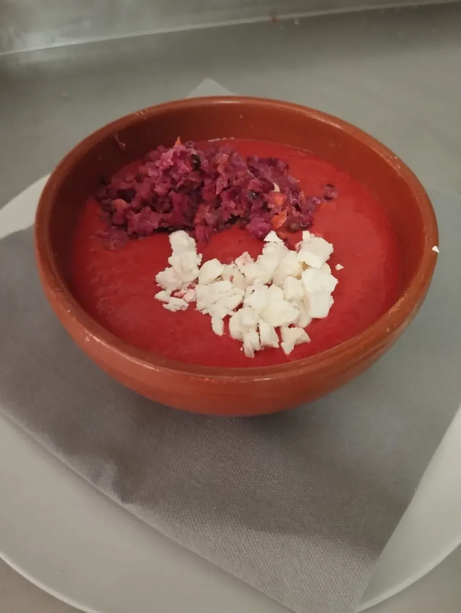 Un tazón de sopa roja cubierto con queso blanco picado y un montón de remolacha rallada sobre una mesa.