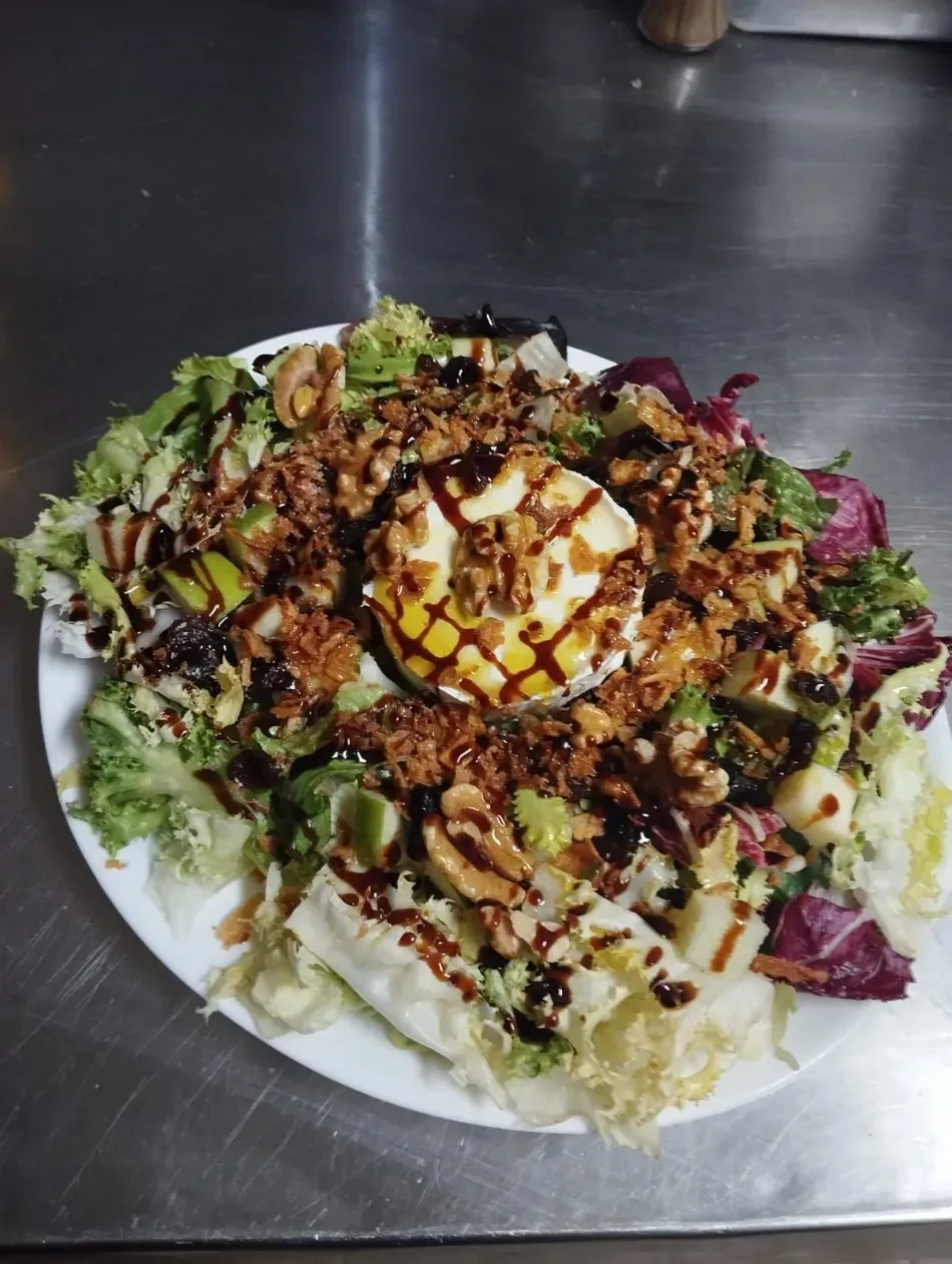 Ensalada fresca con hojas verdes, queso rallado, picatostes y aderezo en un plato blanco.